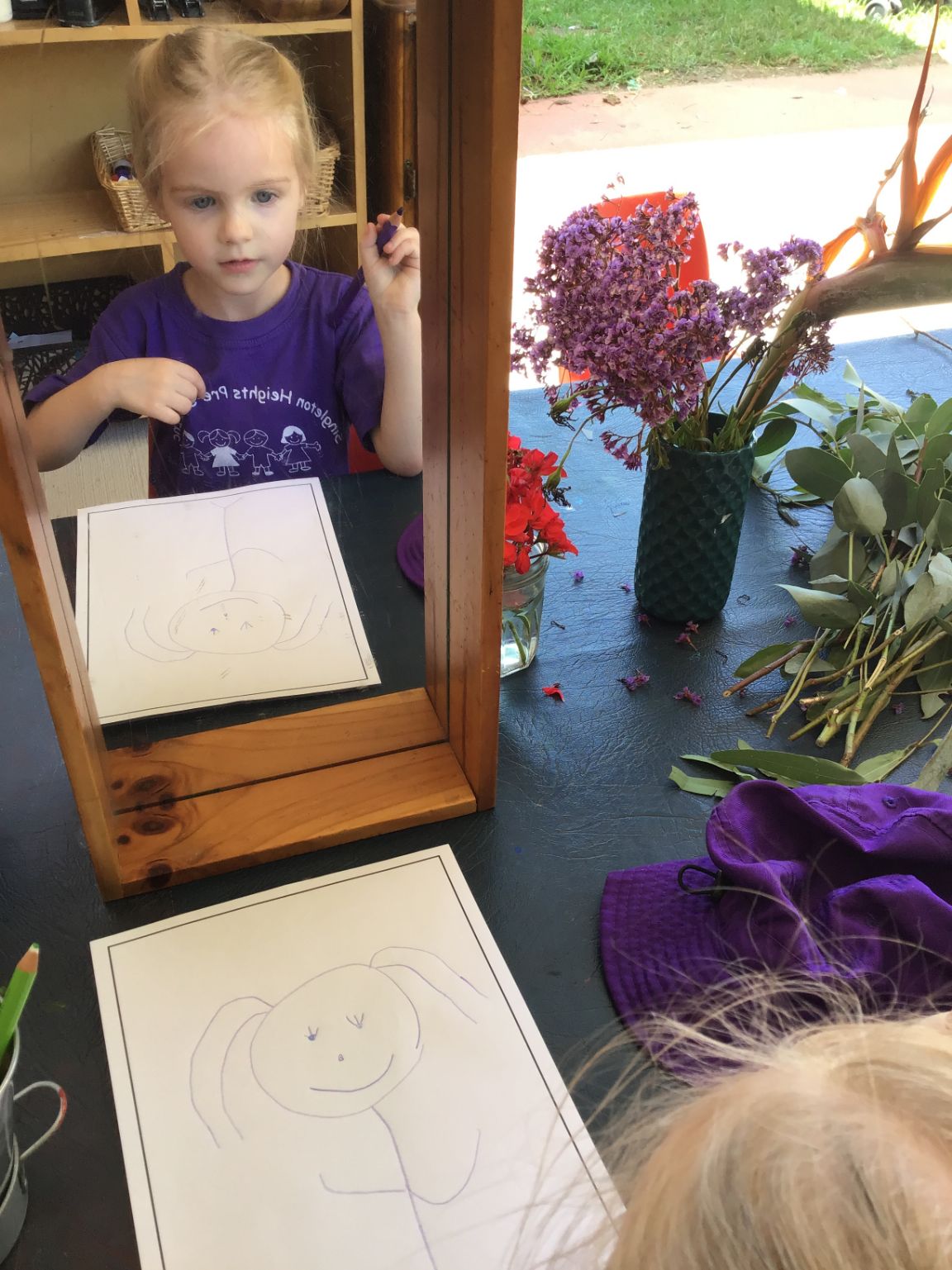 Child drawing a self-portrait in the mirror as part of the five learning outcomes that capture learning and development during early childhood.