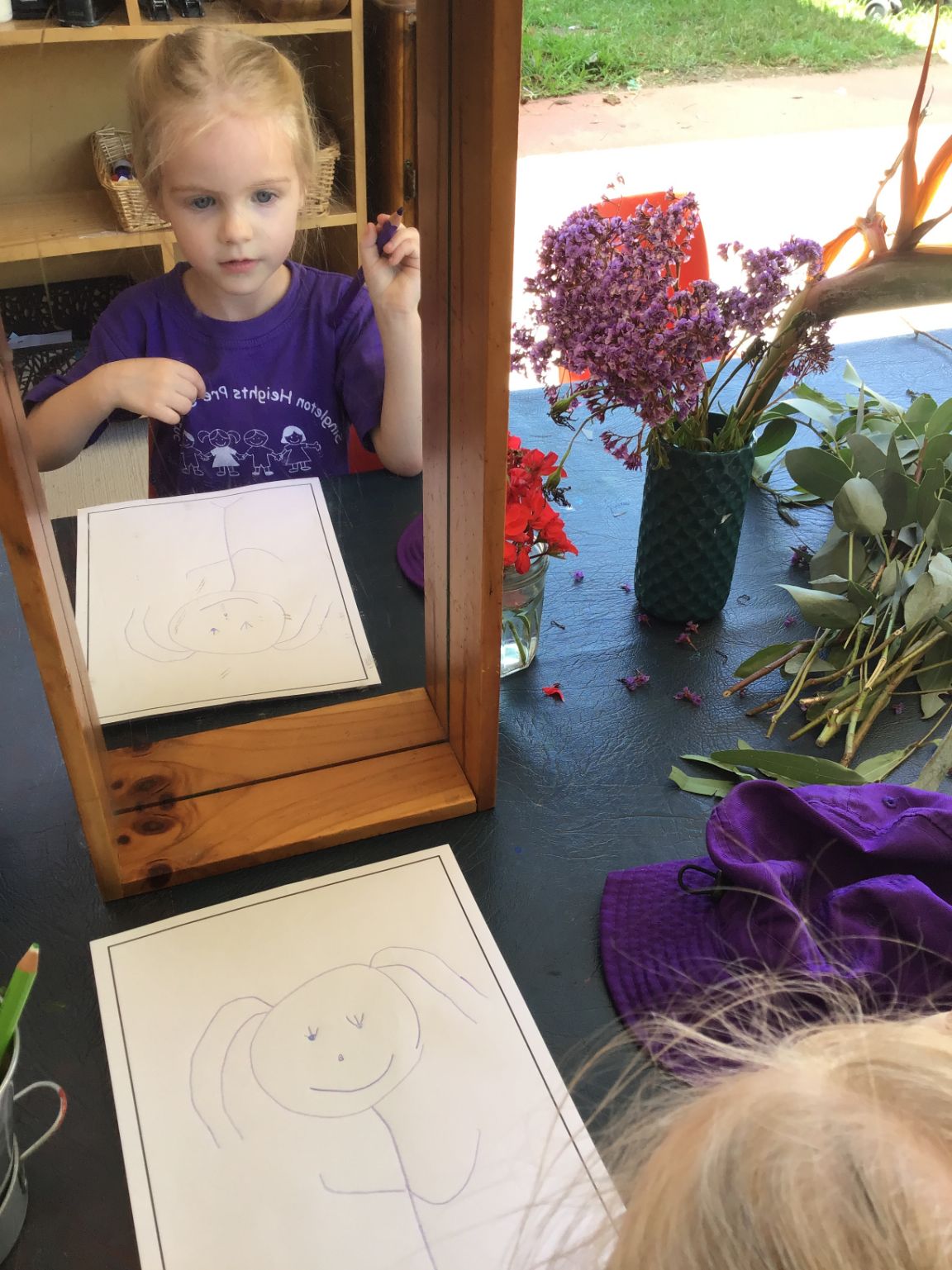 Early Years Learning Framework Child drawing a self-portrait in the mirror as part of the five learning outcomes that capture learning and development during early childhood.